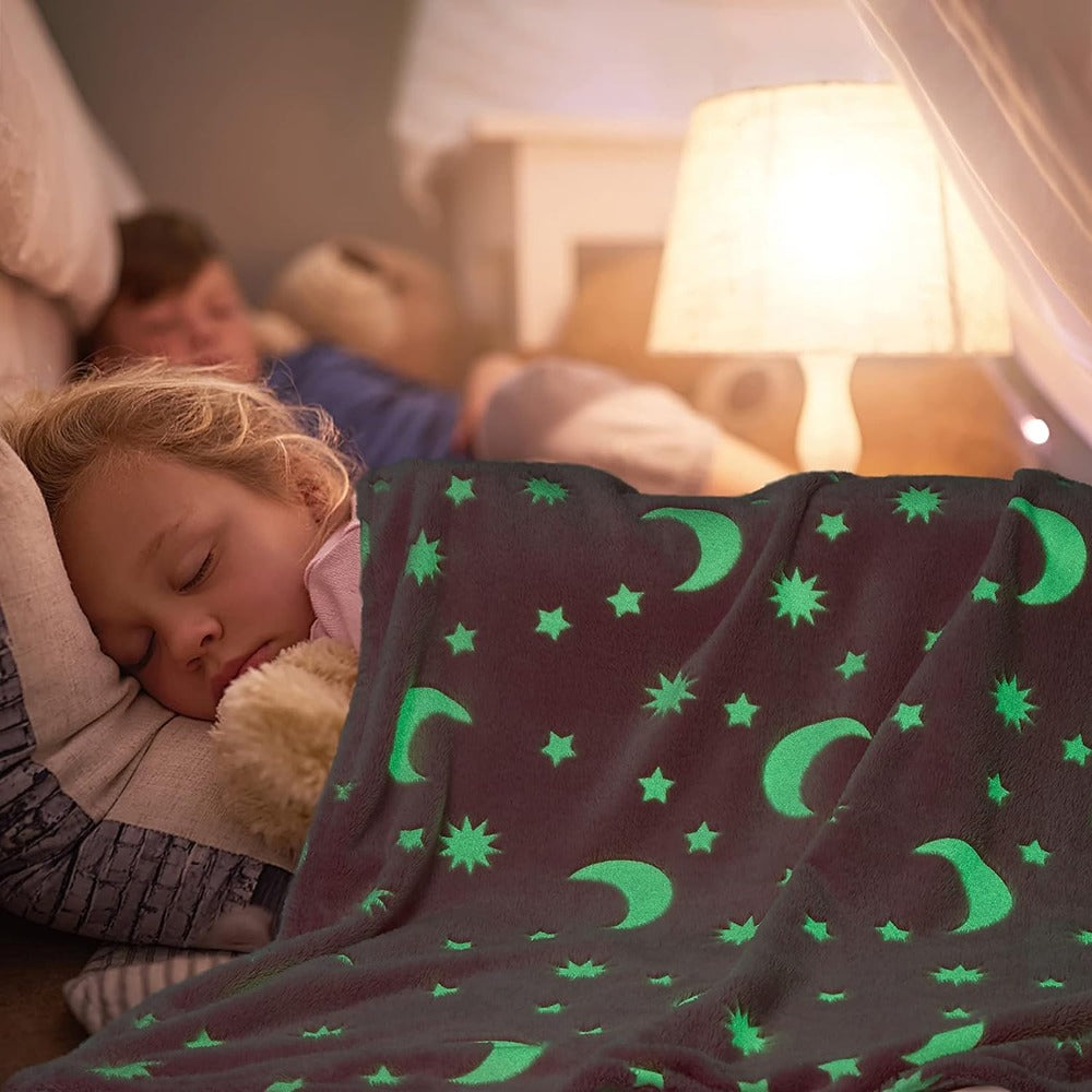 Child sleeping under a glow in the dark moon and stars blanket with a night lamp in the background
