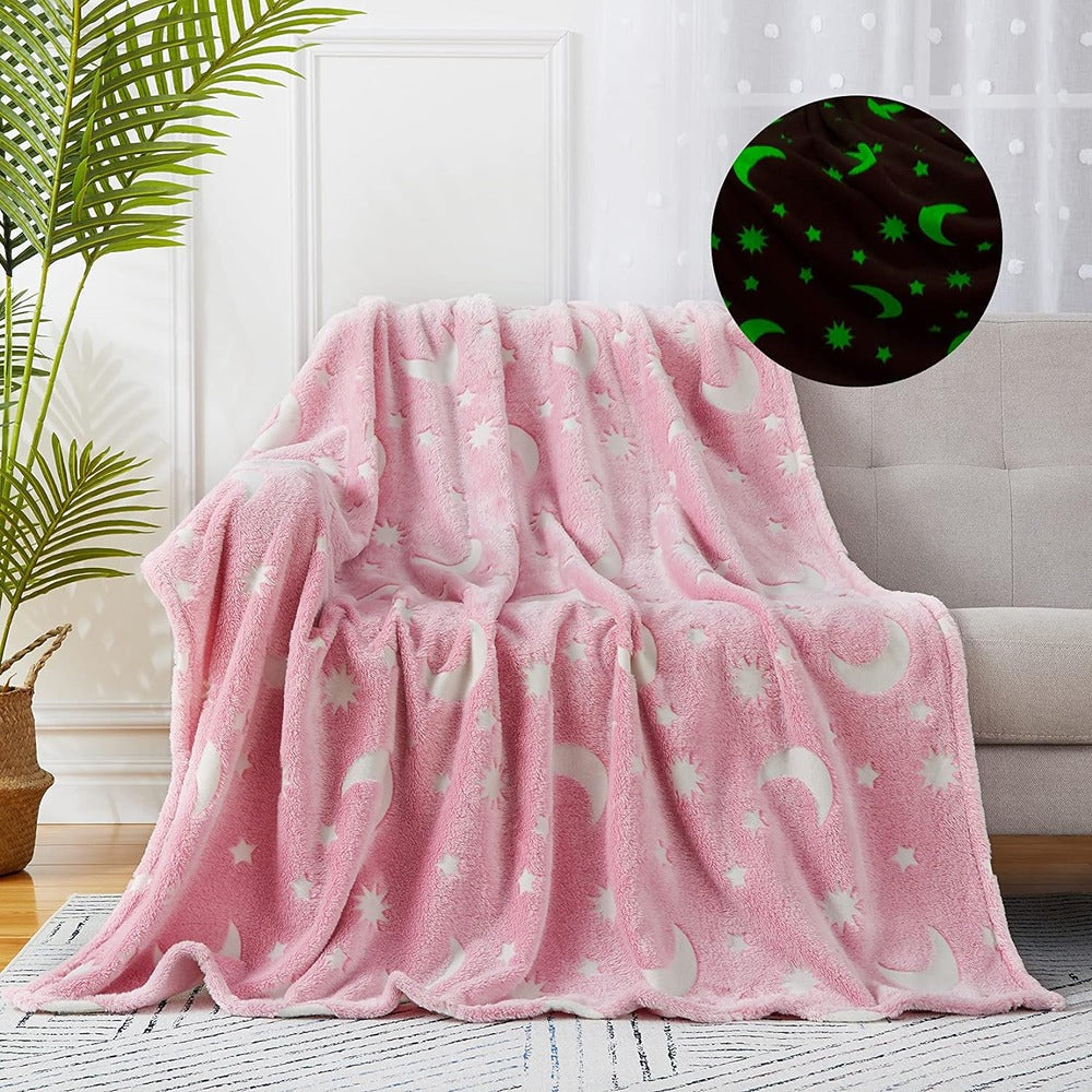 Soft pink glow in the dark fleece blanket with moon and star patterns draped over a sofa