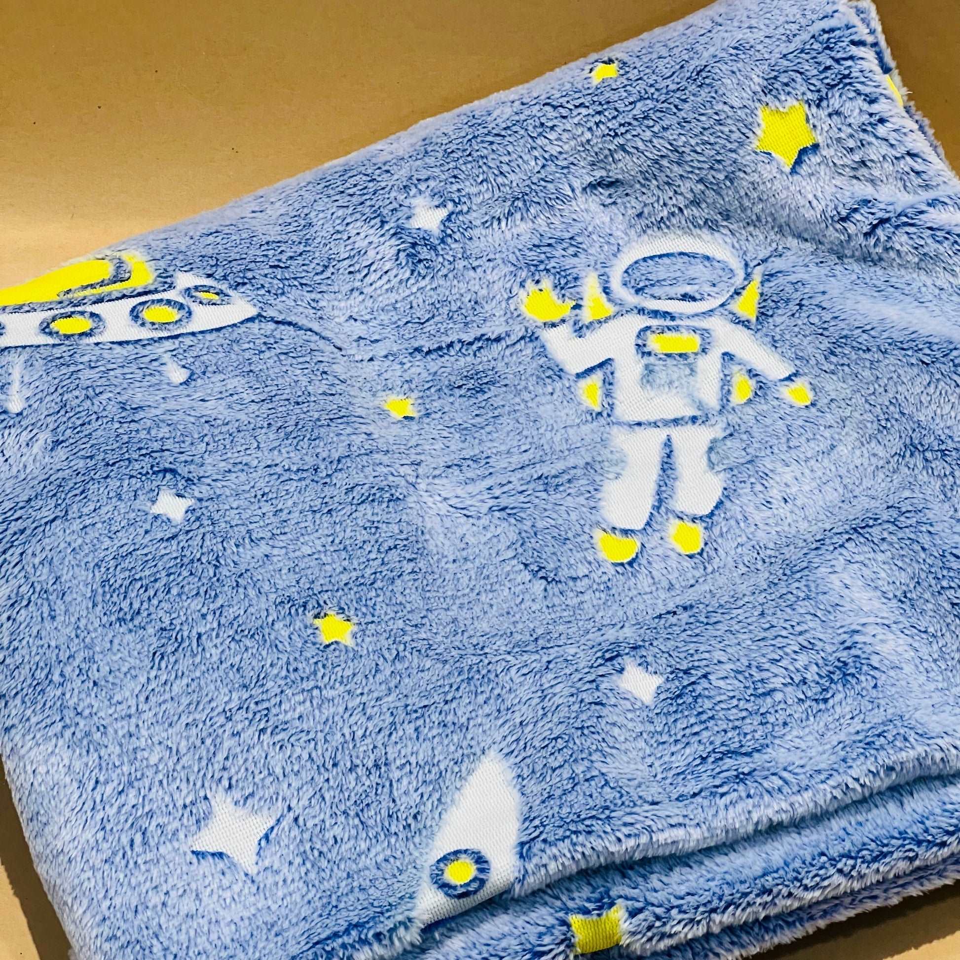 Soft blue fuzzy blanket with yellow and white space-themed designs including astronaut and spaceship