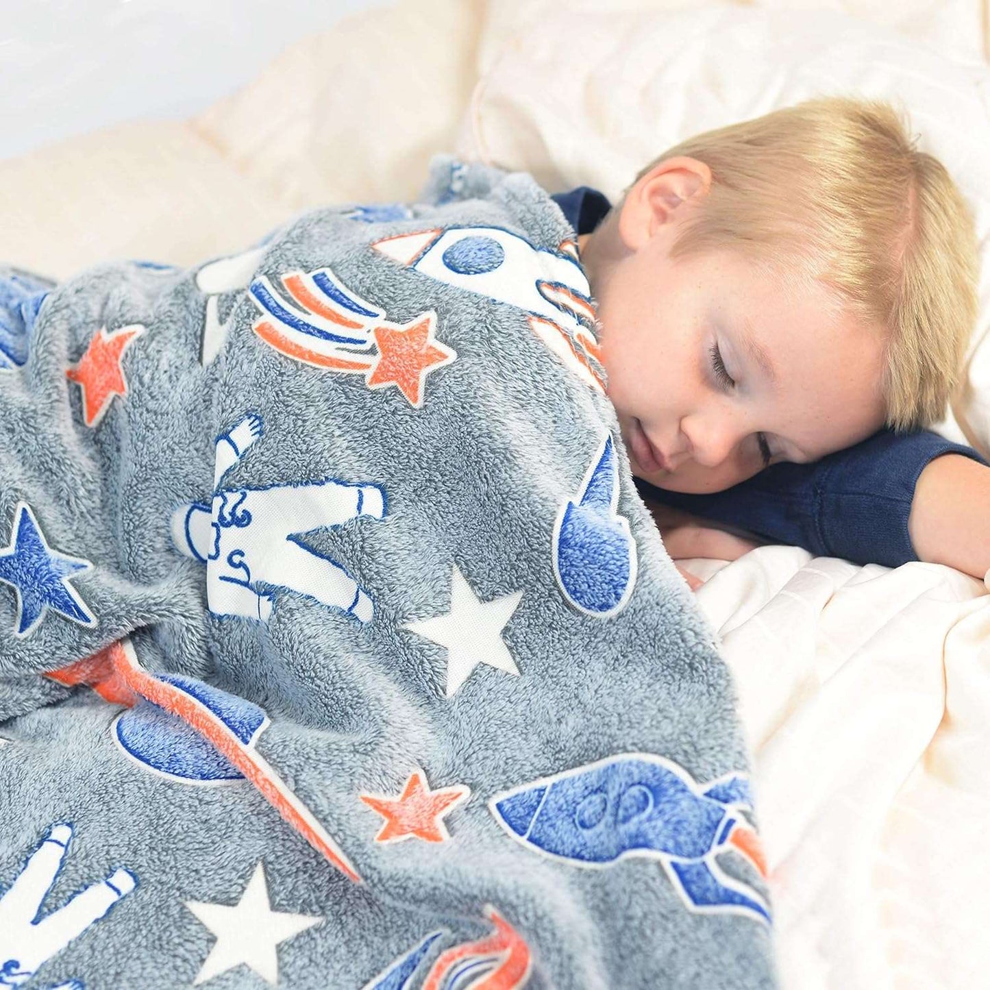 Child sleeping under a gray space-themed blanket with rockets and stars for kids