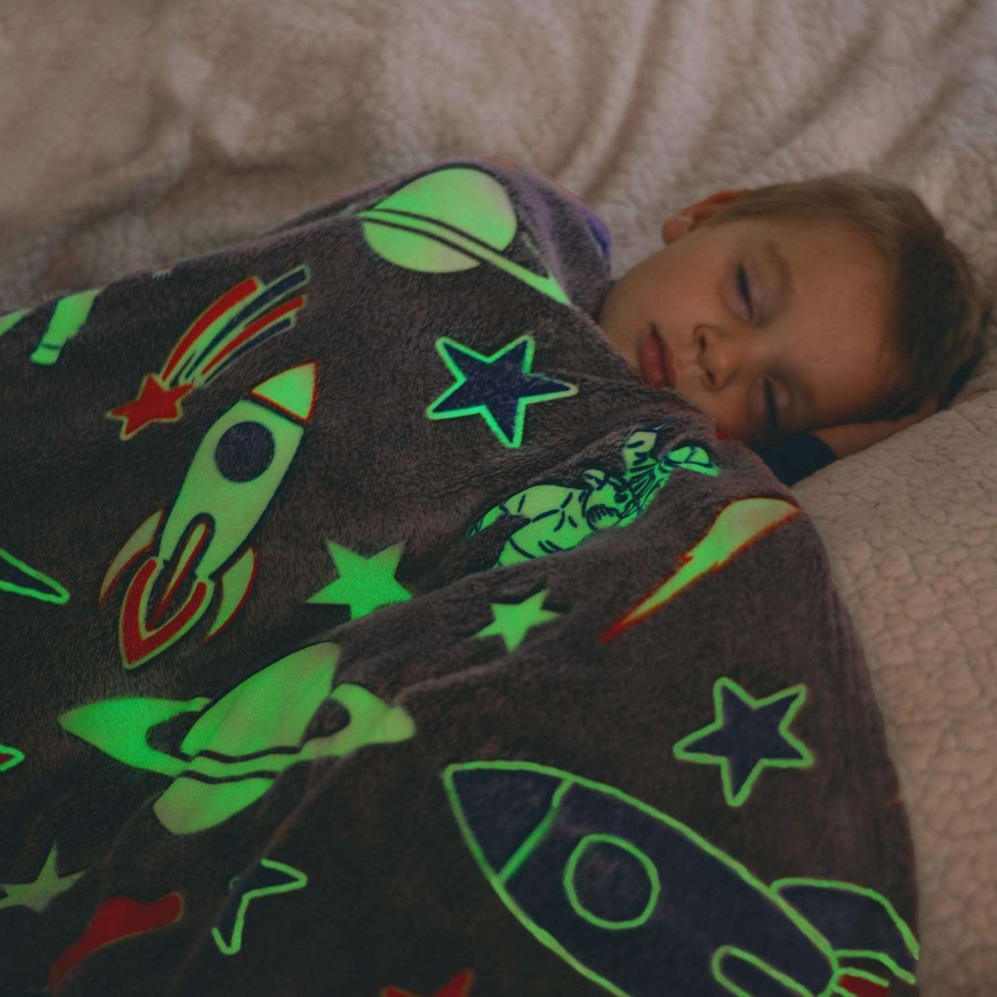 Child sleeping under a dark space-themed glow in the dark blanket with rockets and stars