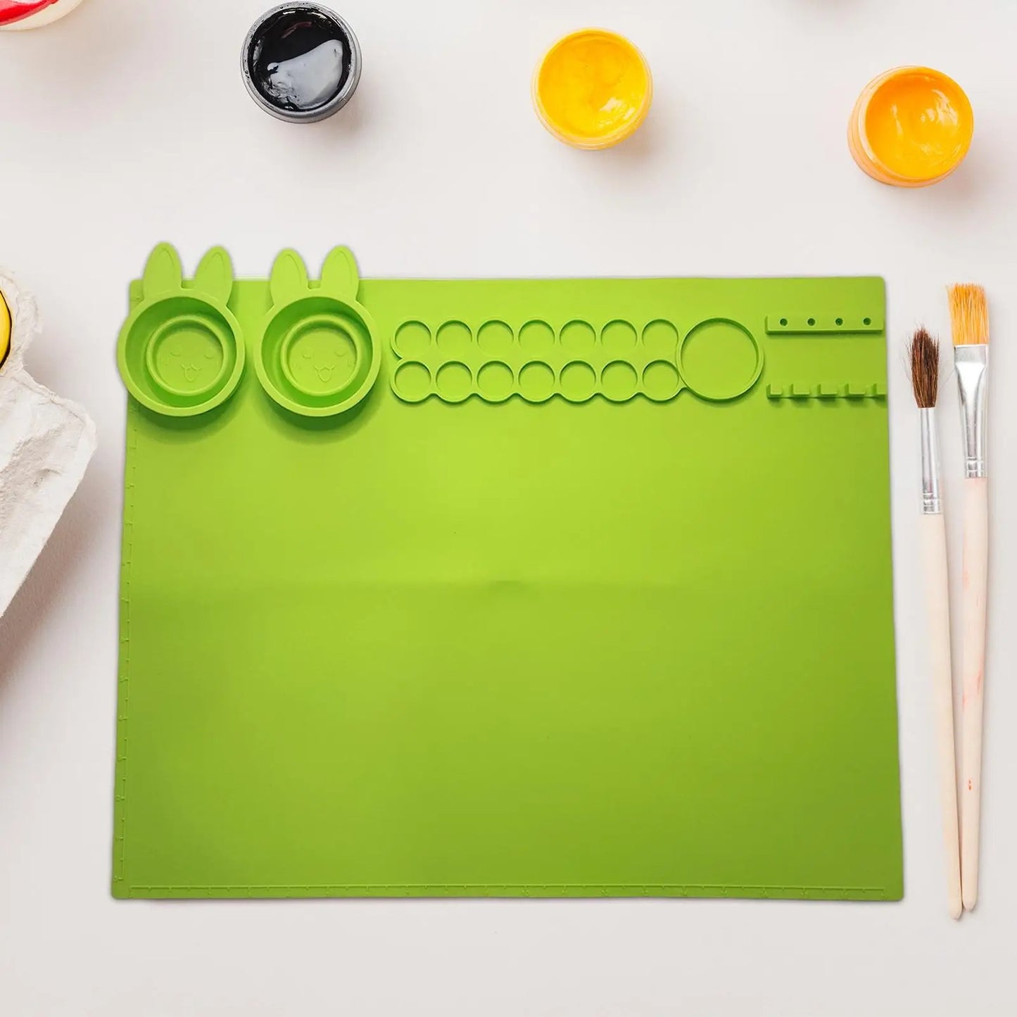 Bright green silicone art mat for kids with various molds and paintbrushes for creative play